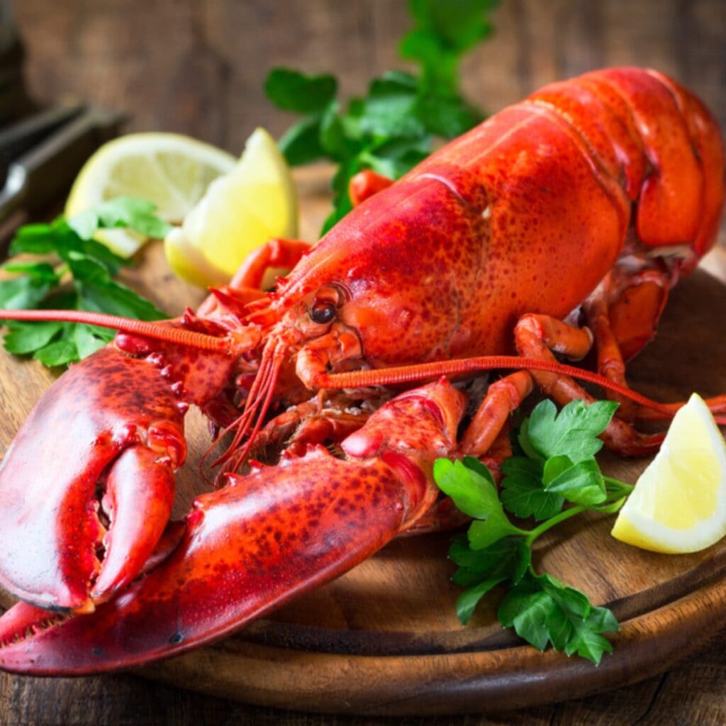 Whole Steamed Lobster Served on a Round Wooden Board Garnished With Slices of Lemon