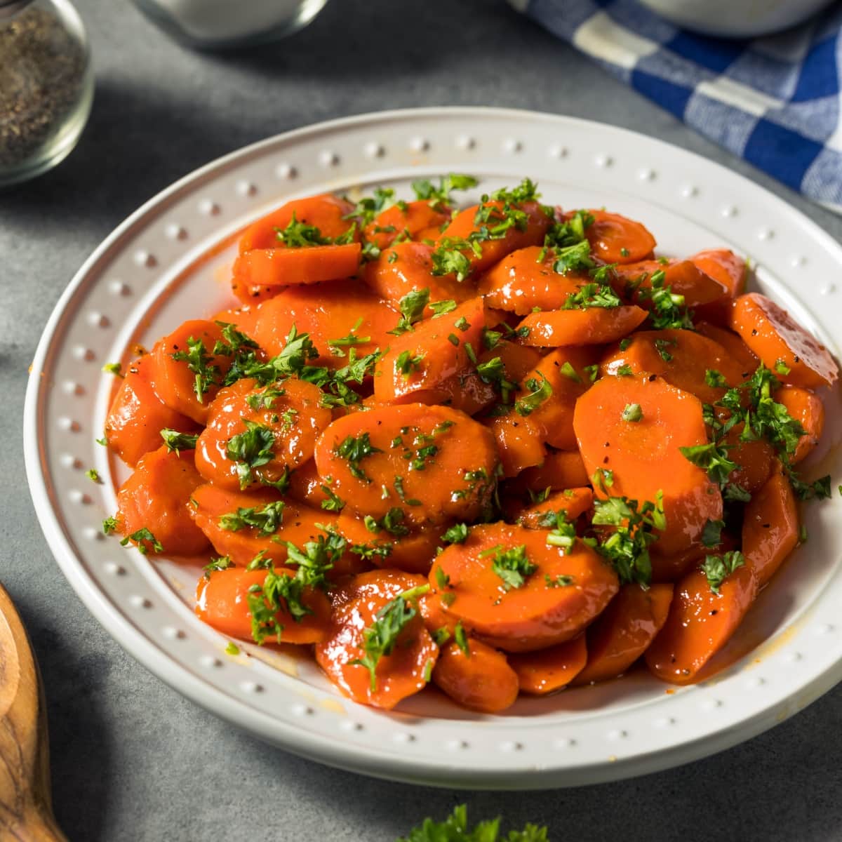 Glazed, Candied Carrots with Parsley on a White Plate with a Wooden Spoon Beside The Plate