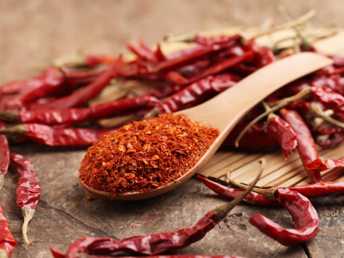 A Spoonful of Cayenne Pepper Powder and Whole Dried Cayenne Peppers on a Wooden Table