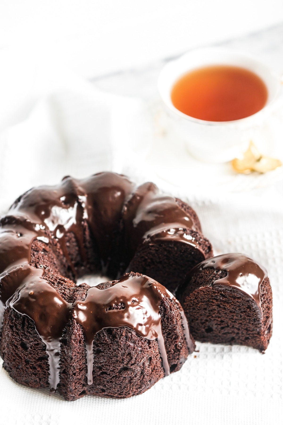 Chocolate Pound Cake (Old-Fashioned Recipe) featuring Chocolate Pound Cake covered in chocolate ganache with a slice taken out of it and a cup of tea in the background.