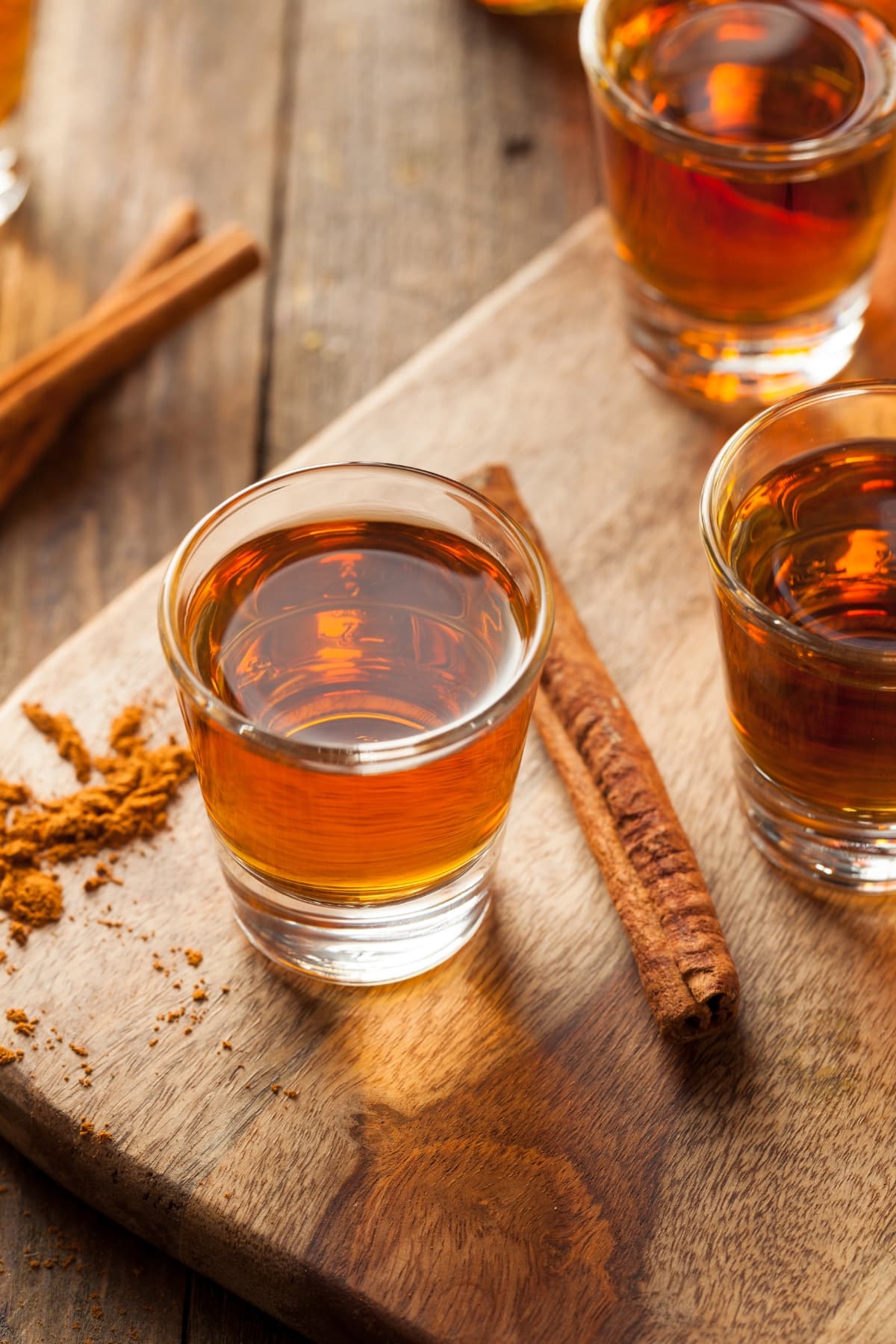 Bourbon vs. Whiskey- The Main Differences featuring Cinnamon Bourbon Whiskey in 3  Shot Glasses on a cutting Board with a Cinnamon Stick and Ground Cinnamon