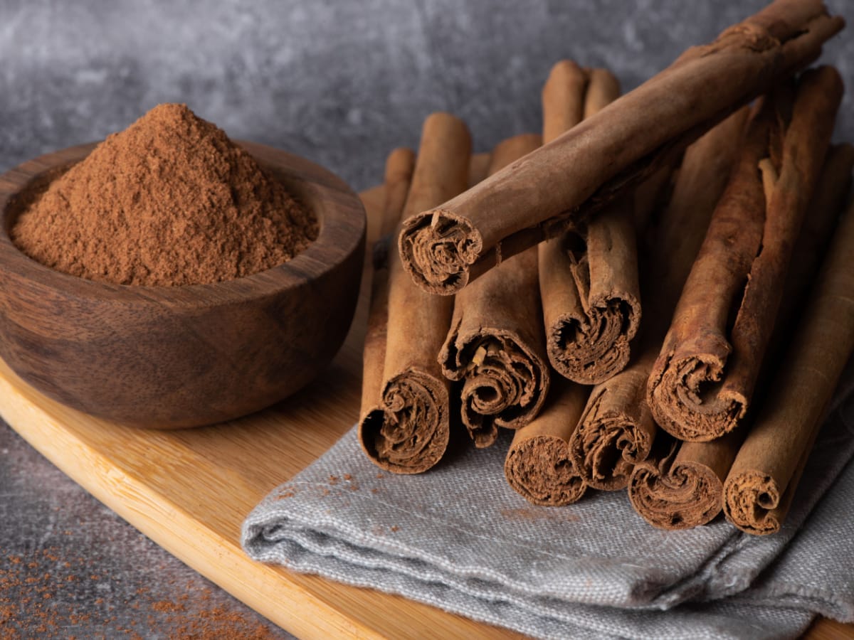 A Bowl of Cinnamon Powder and Bunch of Cinnamon Sticks on a Cloth on a Wooden Board