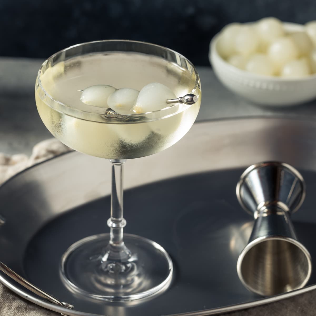 Savory Gibson Cocktail in a Wine Glass with Cocktail Onions on a Skewer for Garnish on a Silver Serving Tray, Alcohol Measurer Beside 