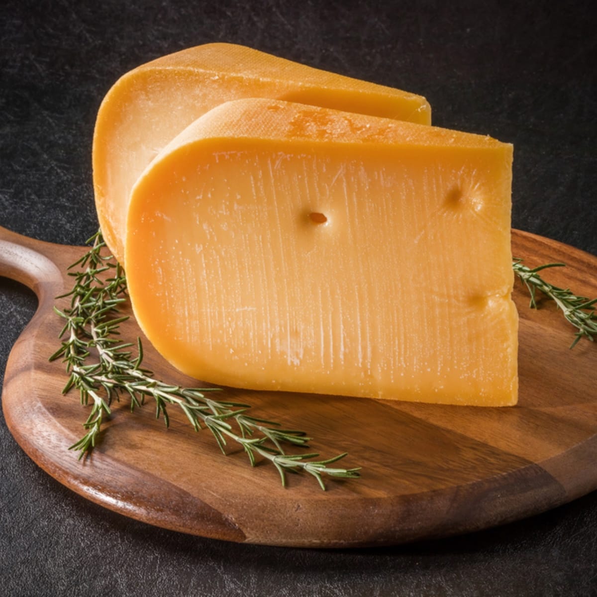 Two Chunks of Gouda on a Cutting Board with Rosemary