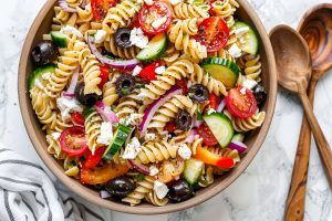 Top View of Greek Pasta Salad in a Bowl with Two Wooden Spoons to the Side