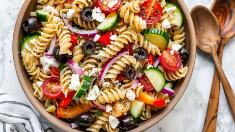 Top View of Greek Pasta Salad in a Bowl with Two Wooden Spoons to the Side