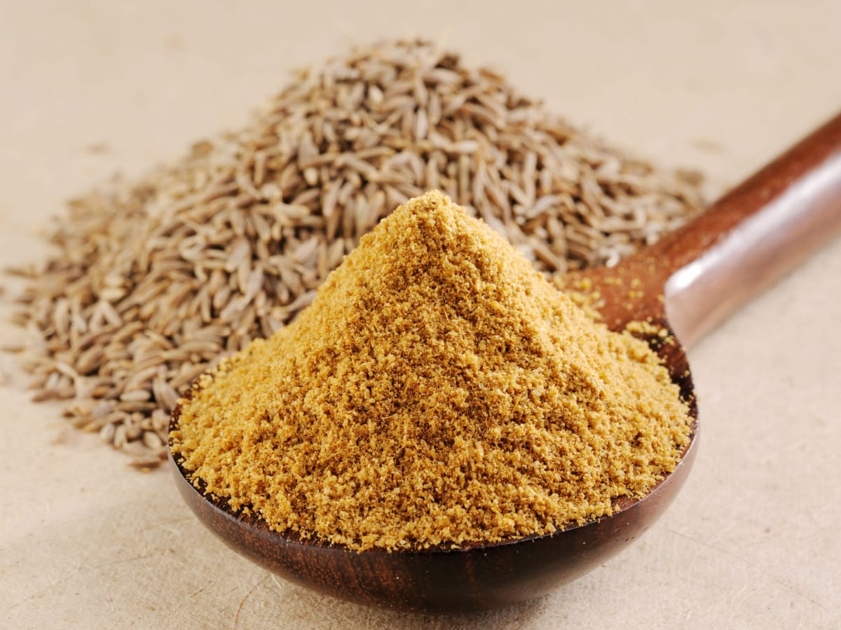 Heap of Ground Cumin on a Wooden Spoon with a Heap of Whole Cumin Seeds Behind It