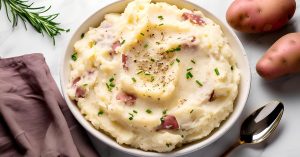 A bowl of homemade mashed red potatoes with herbs and truffle oil and a sprig of rosemary