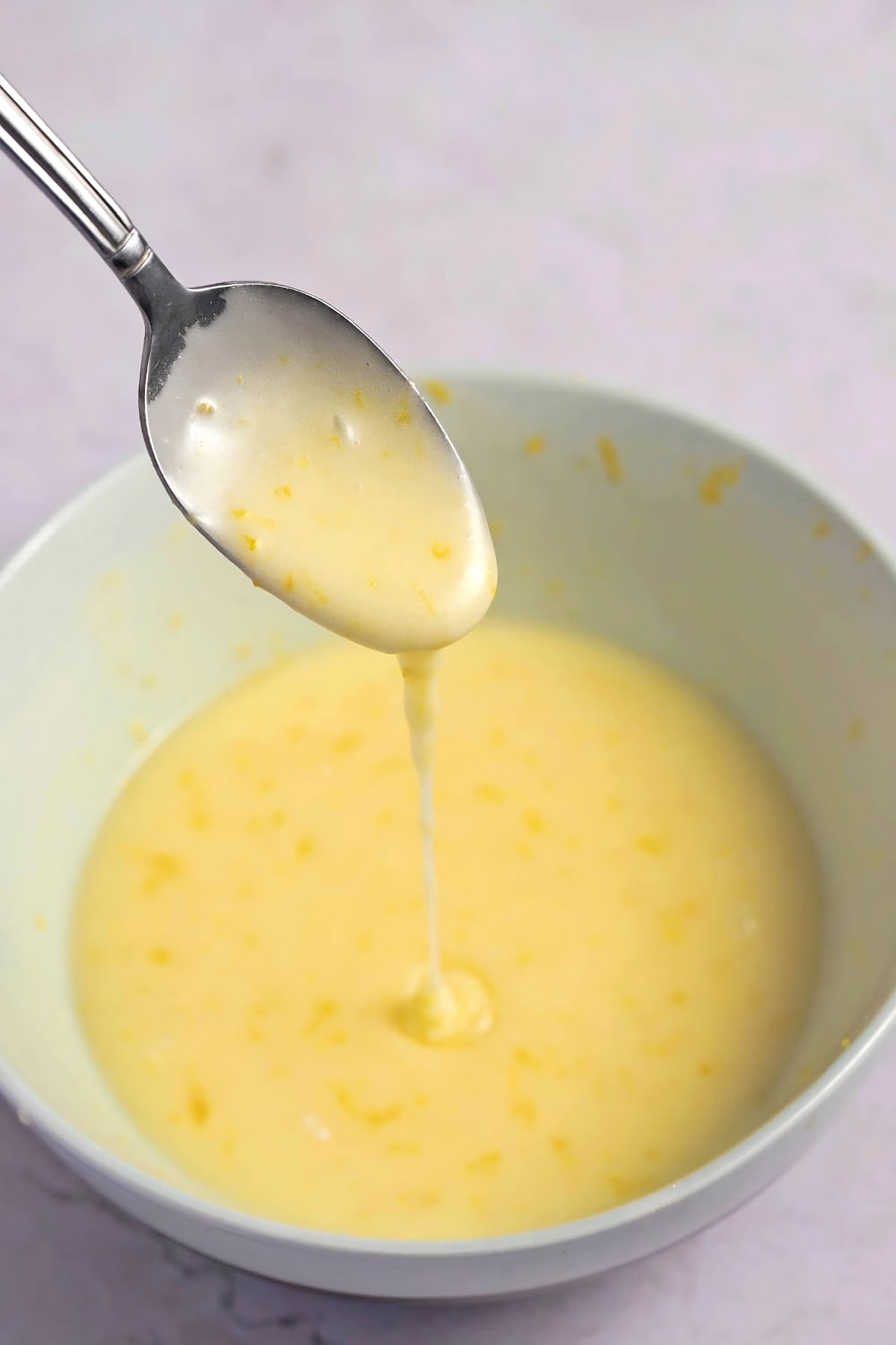 Orange Glaze Icing Dripping From a Spoon into a White Bowl