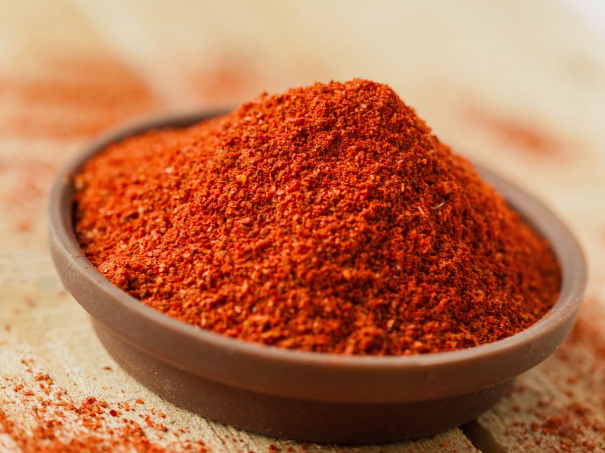 Dry Organic Red Smoked Paprika in a Bowl on a Wooden Table with Paprika Around the Bowl