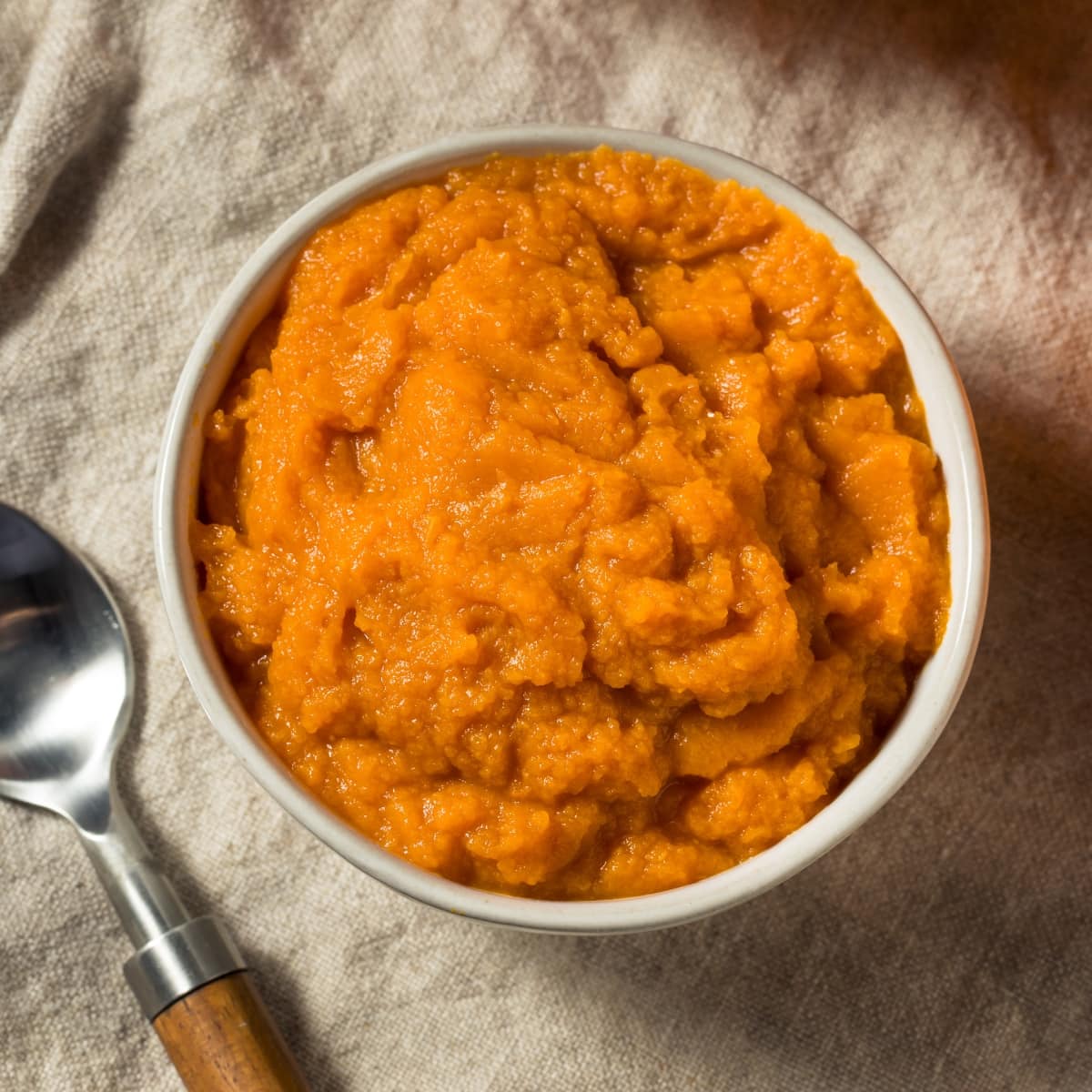 Pumpkin Puree in a Glass Bowl on a Rustic Cloth with a Spoon Next to the Bowl