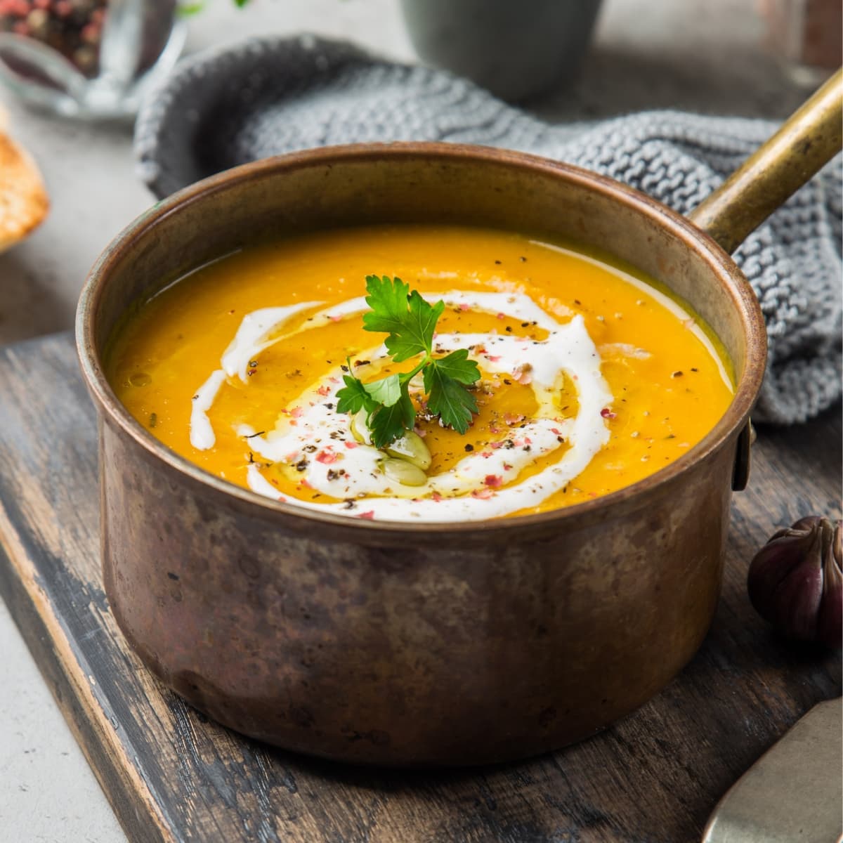 Pumpkin Soup Made From Pumpkin Puree with Seasonings, Oil, Cream, and Parsley on Top  in a Metal Pot on a Wooden Table