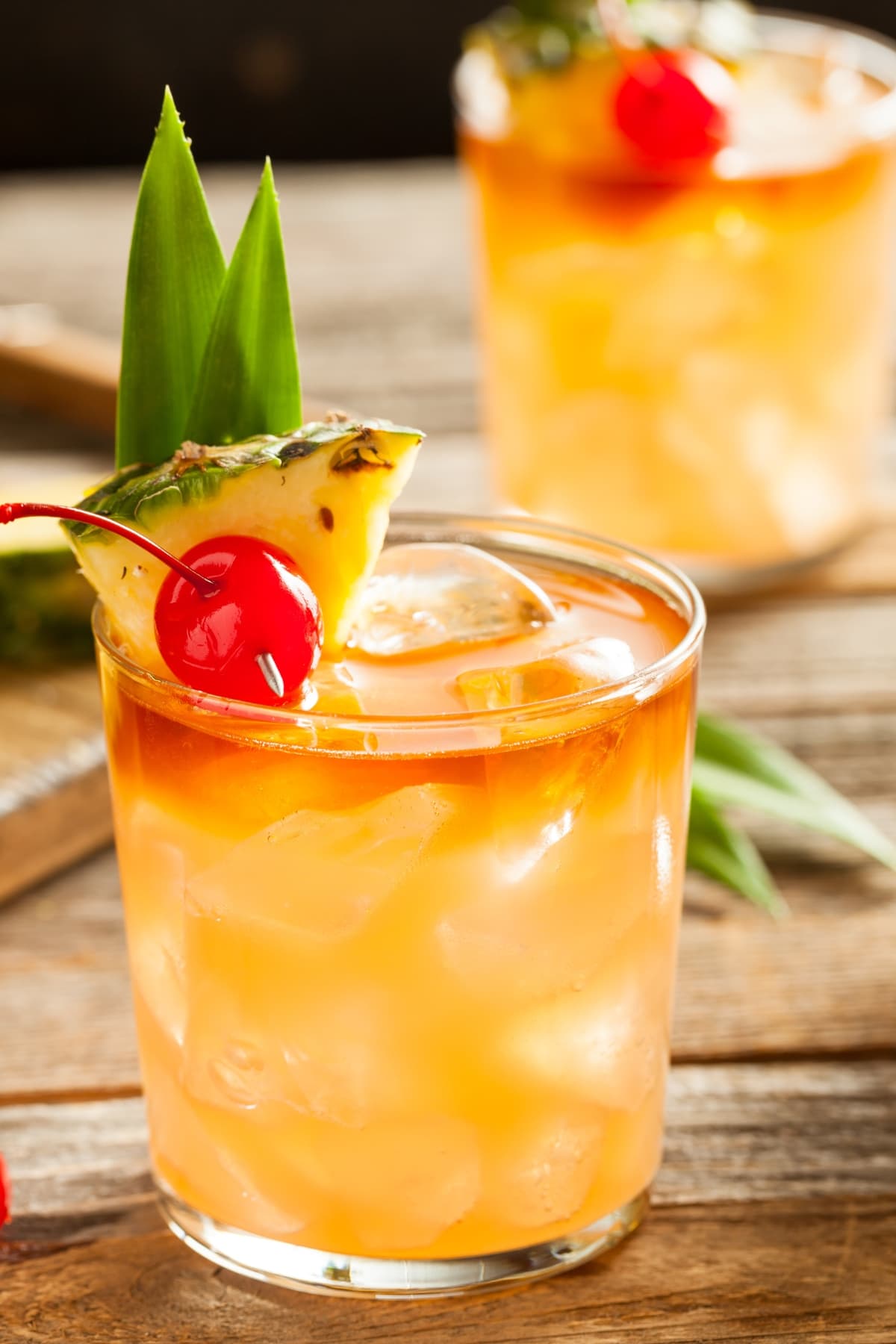 Classic Mai Tai Cocktail (Best Recipe) featuring Two Glasses of Refreshing Mai Tai Cocktail with a Pineapple, Cherry, and Leaf Garnish