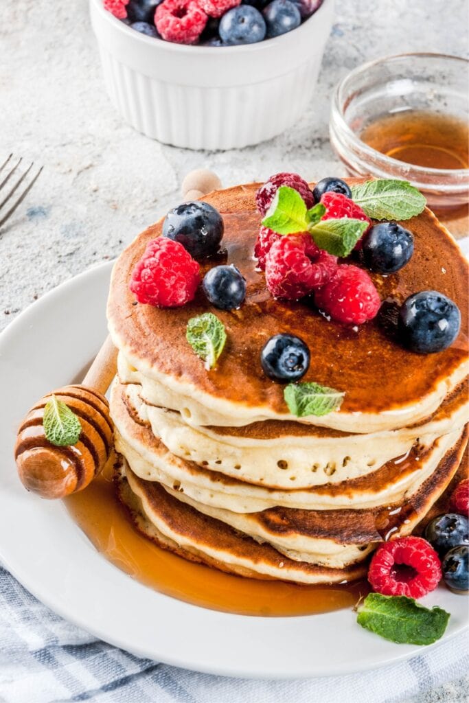 Easy, Fluffy Oat Flour Pancakes (Best Recipe) featuring Plate Stacked With Homemade Oat Flour Pancakes with Fresh Berries, Honey, and Mint on Top