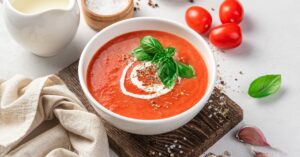 Tomato soup in a bowl garnished with basil and cream, creating a visually appealing and appetizing dish