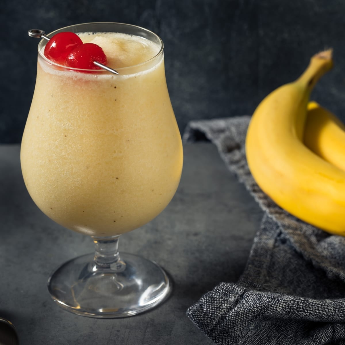 A Glass of Banana Daiquiri Cocktail with Two Ripe Bananas in Side