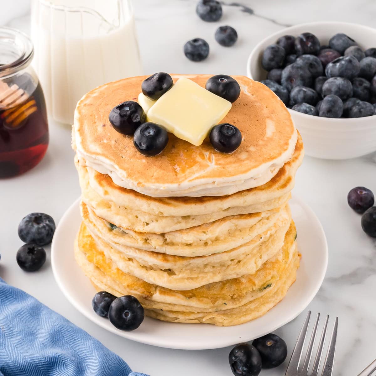 Stack of blueberry pancakes with butter and blueberries on top.