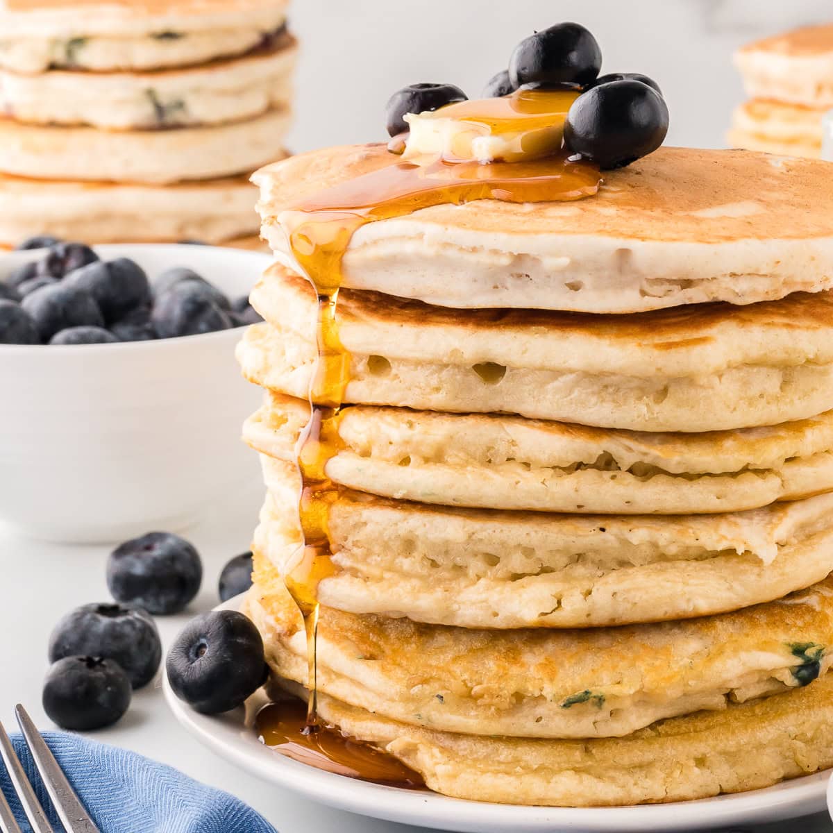 Blueberry Pancakes with butter and maple syrup. Bowl of blueberries in the background. Close-up shot.