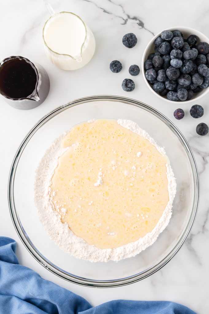 Pancake ingredients combined in a glass bowl. Bowl of fresh blueberries on the side.