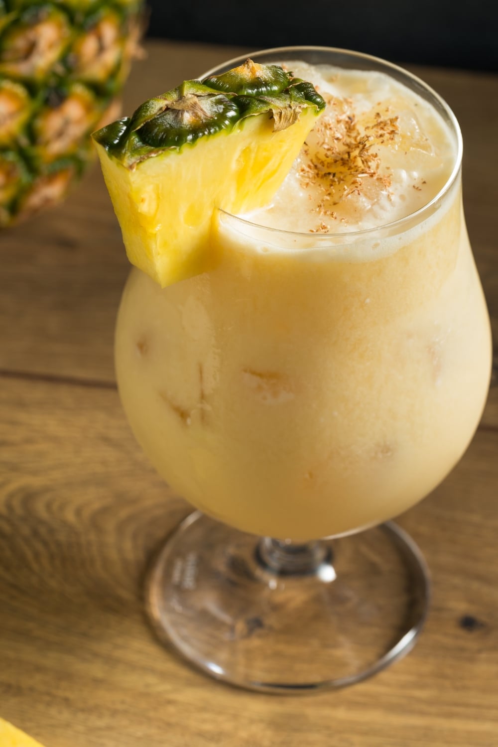 A glass of Pineapple Cocktail with a pineapple garnish on a wooden table