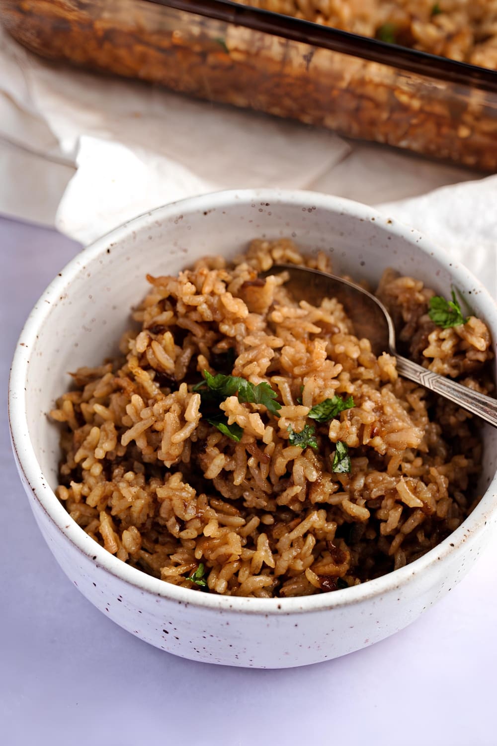 Brown colored rice in a white bowl with spoon. 