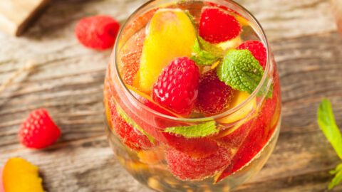 Close up view of a glass of white sangria with peaches and raspberries