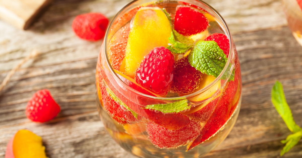 Close up view of a glass of white sangria with peaches and raspberries