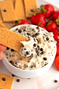 Dipping Wafer into Cheesecake Dip with Chocolate Chips and Fresh Strawberries