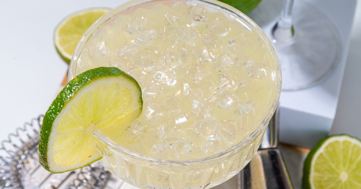 Close up shot of a gimlet cocktail filled with ice and garnished with lime wheel