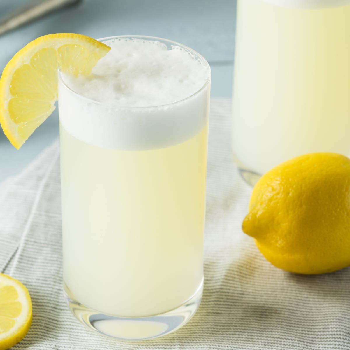 Fresh lemon and glass of bubbly gin fizz on a table garnished with half lemon wheel slice, with a bright yellow lemon on side