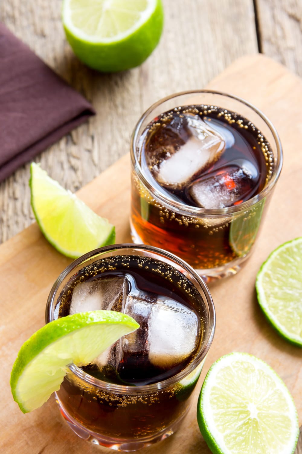 Glasses of Cuba Libre on a Wooden Board with Lime and Ice