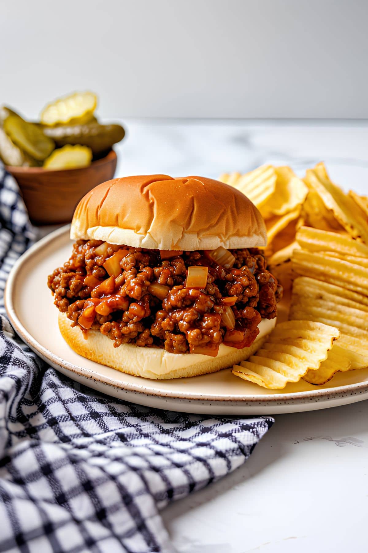 Sloppy Joe with Chips sitting on a white plate, pickles in the background