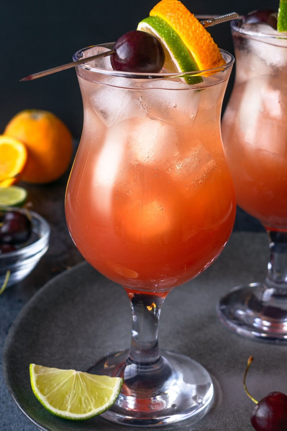 Two Hurricane Cocktails Garnished with Cherry, Lime, and Orange Slice