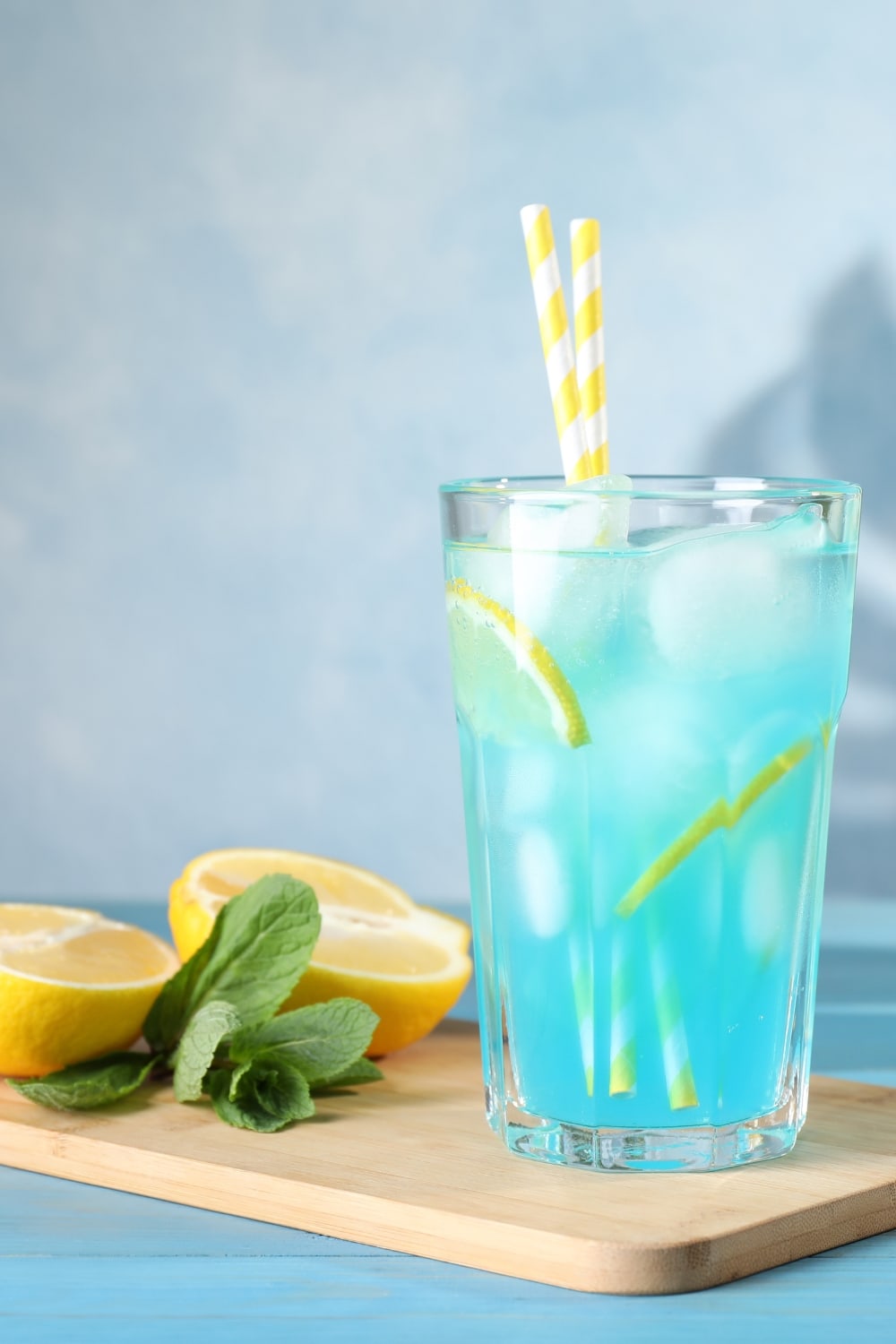 A glass of refreshing and ice-cold Blue Lagoon Cocktail with lemon wheel slices, and fresh mint