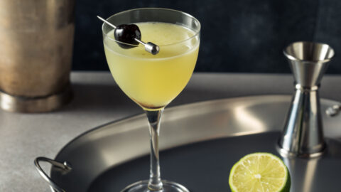 A jigger, lime slice and a glass of a last word cocktail on a metal tray