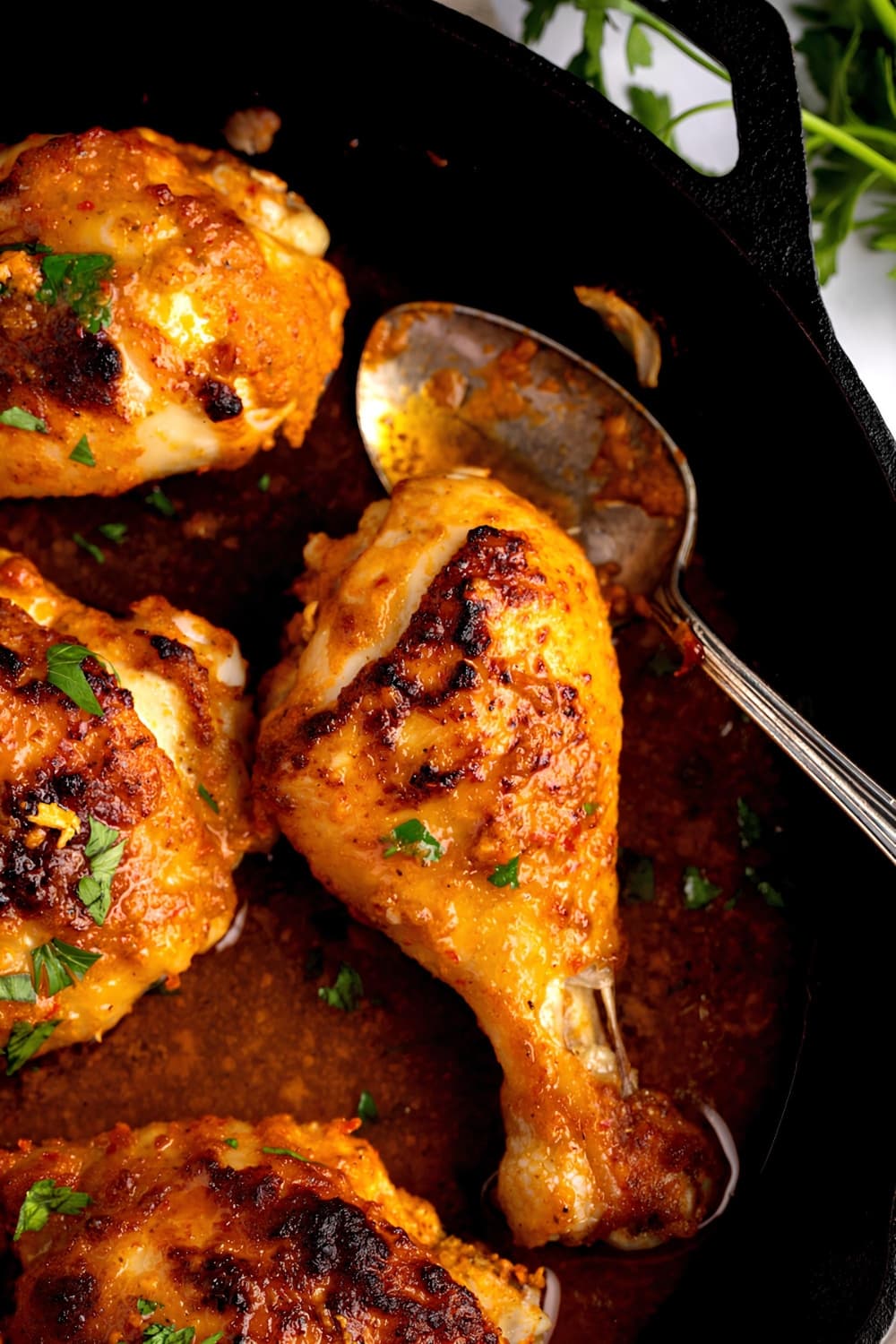 Peri-Peri Chicken cooked in an iron cast, with sauce and herbs and spoon dipped on it. 