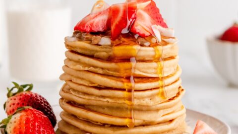Pouring Maple Syrup on a Pancake with Fresh Strawberries on Top