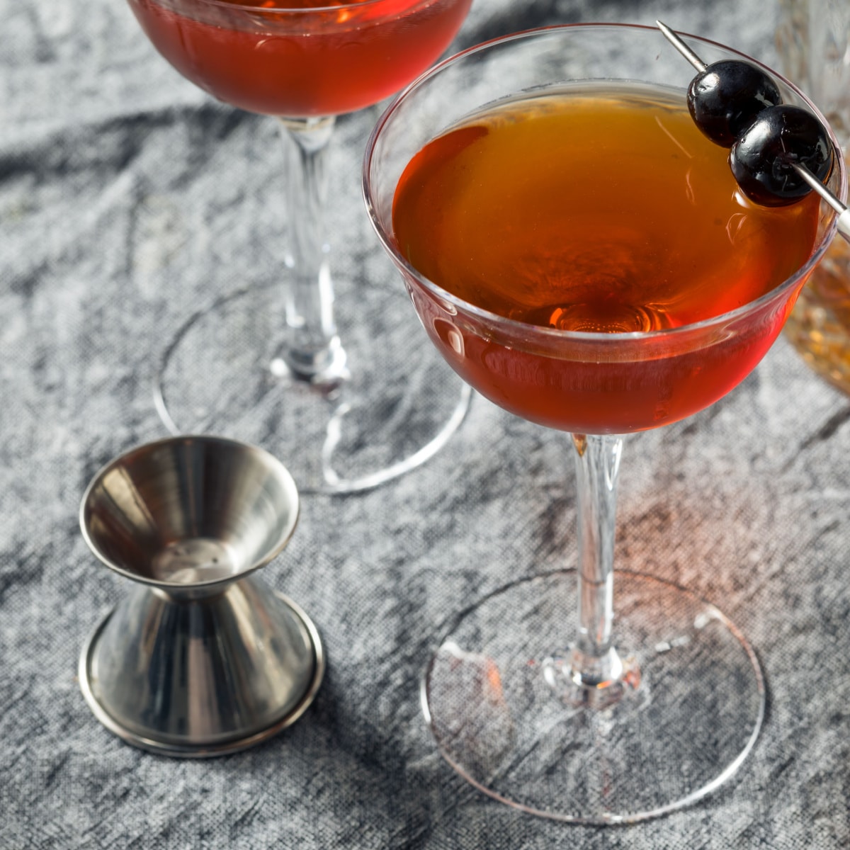 Rob Roy Cocktail on a stemmed glass with jigger and cocktail strainer on a wooden table
