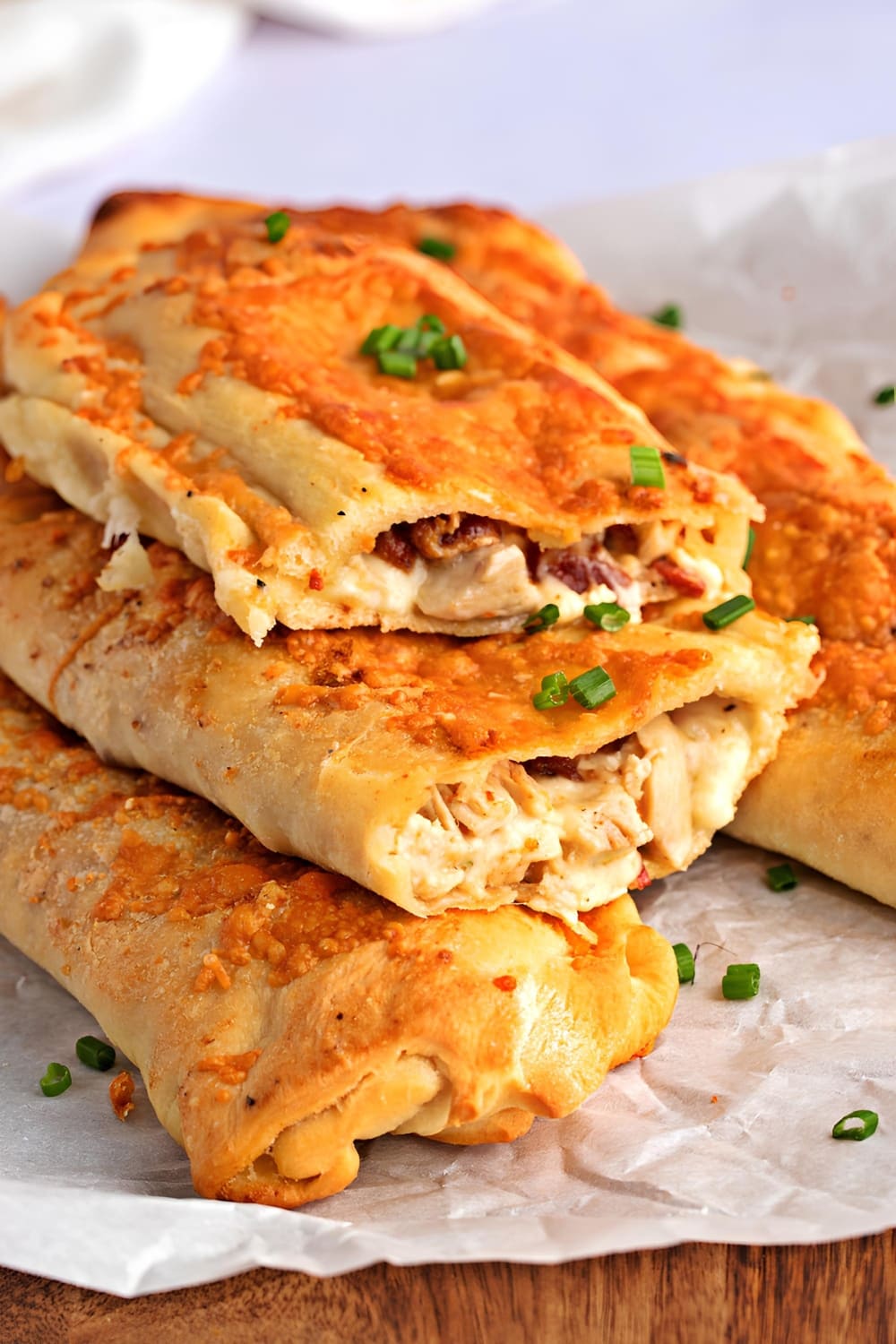 Whole and sliced in a half Costco Chicken Bake, stacked on a parchment paper, on top of a wooden table, garnished with chopped onions