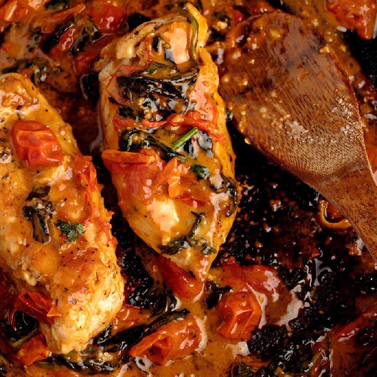 Tuscan Chicken in tomatoes and spinach cook with a wooden spoon and skillet 