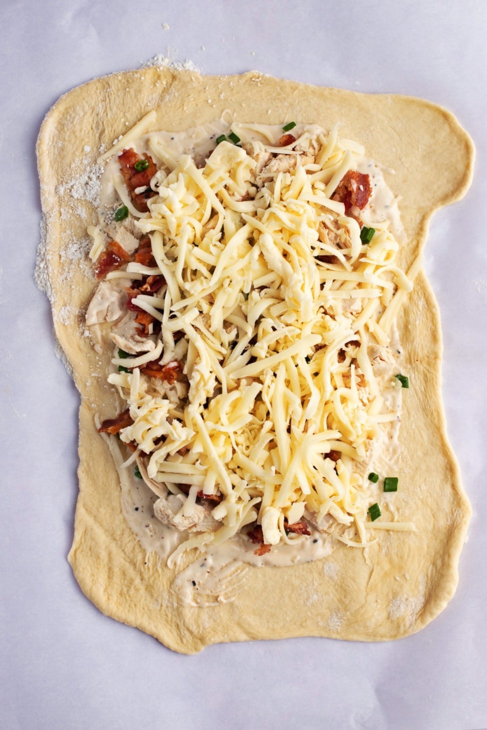 Raw dough, flat on a table, topped with Costco Chicken bake ingredients, dressing, chicken, bacon, cheese, seasonings and 