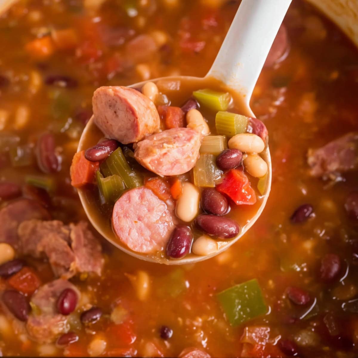 A laddle filled with 10-bean soup with ham and ham hock, close-up.