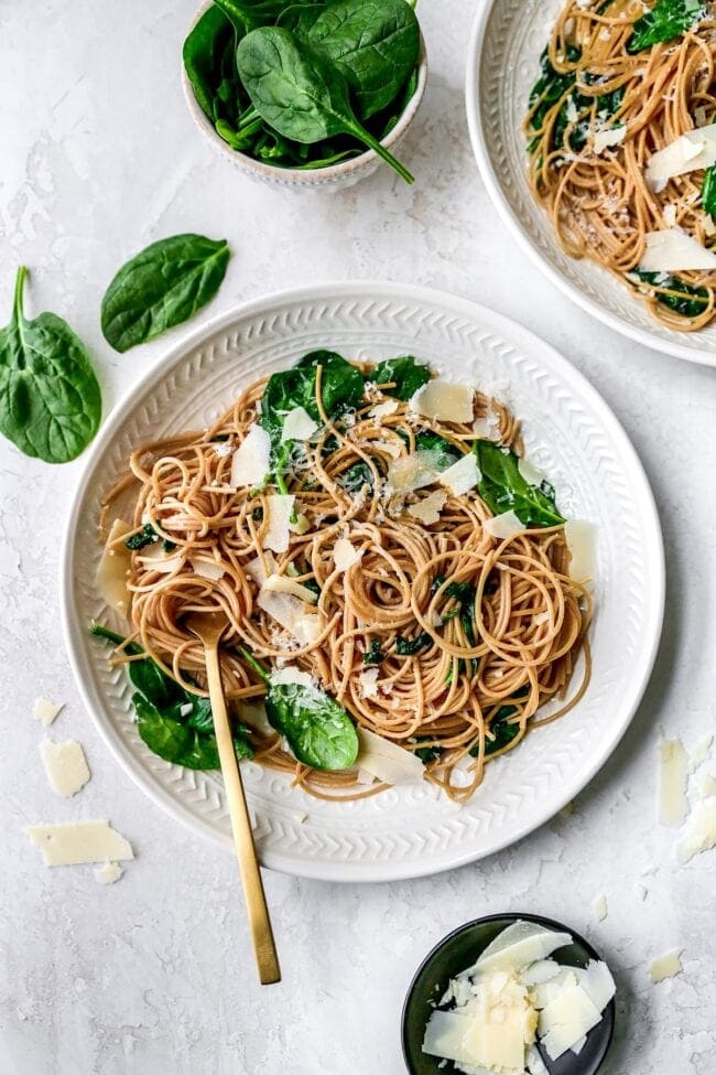 A plate of spaghetti topped with spinach and parmesan cheese