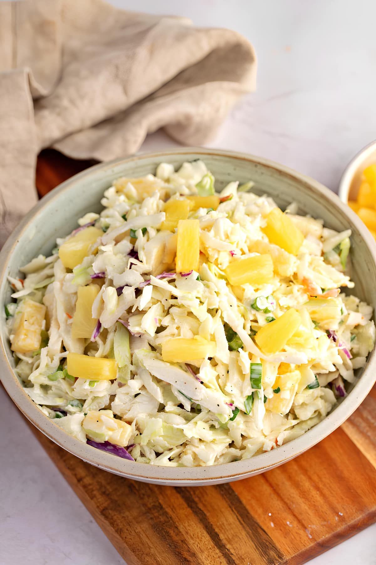 A Bowl of Coleslaw with Pineapple on a Wooden Cutting Board