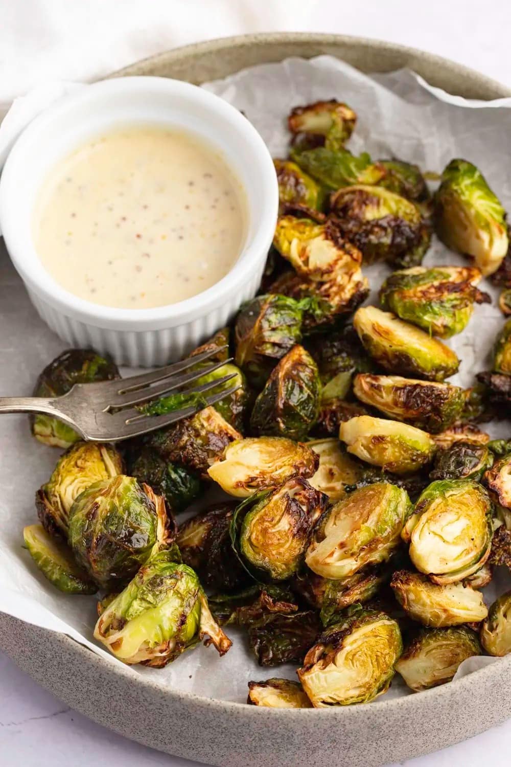 Roasted brussels sprout on a plate with creamy dip on side. 