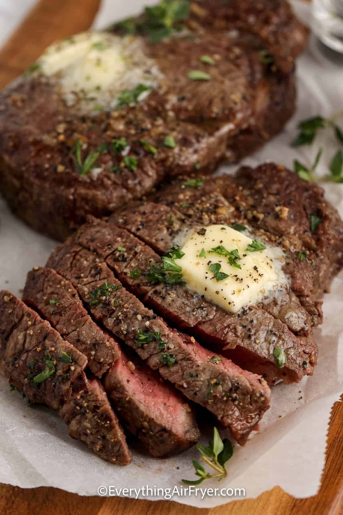 Air Fryer Steak sliced on a wooden cutting board with parchment paper garnished with parsley topped with butter