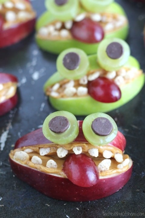 Sliced apple designed as cute monsters with grapes, butter and chocolate chips. 
