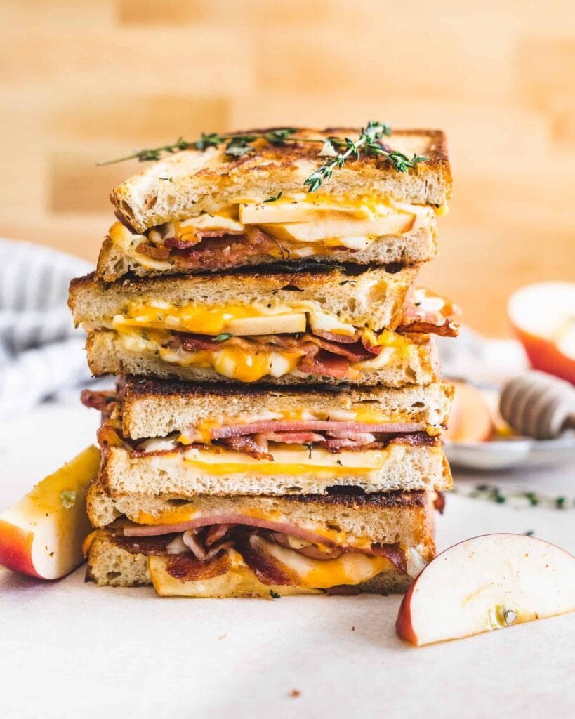 Stack of bacon and apple grilled cheese sandwich slice in half.