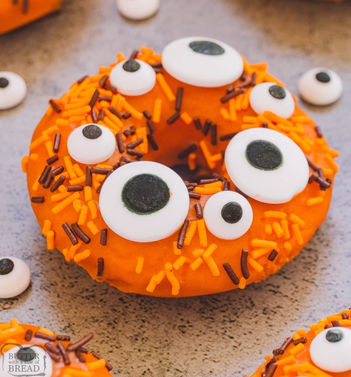 Orange colored donut decorated with candy eyes and chocolate and orange sprinkles. 