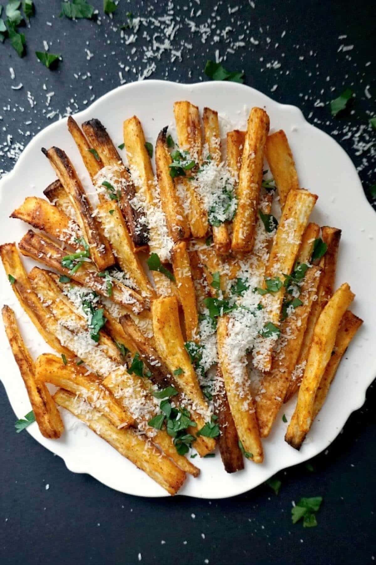 Baked parsnip fries on a plate garnished with parmesan cheese. 